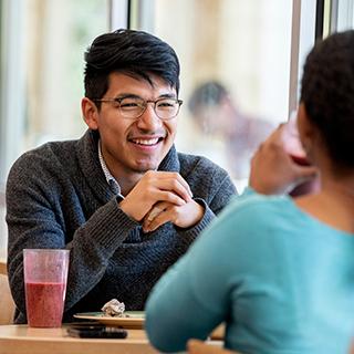 在市场广场，一位戴眼镜的年轻男学生隔着桌子朝一位年轻女子微笑, TCU主餐厅.